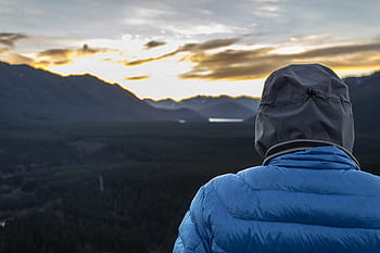 person, wearing, blue, bubble jacket, looking, sunset, bubble, jacket, standing, near, mountains