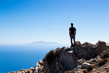 man, standing, rock, overlooking, island, straight, mountain, peak, near, sea, daytime