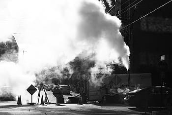 grayscale photo, smoke, construction, signs, pylons, street, road, block, cars, smoke - physical structure, built structure