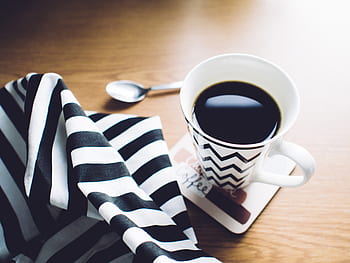 coffee, morning, black and white stripes, coffee cup, wooden table, spoon, napkin, zigzag pattern, hot beverage, cozy atmosphere, breakfast setting