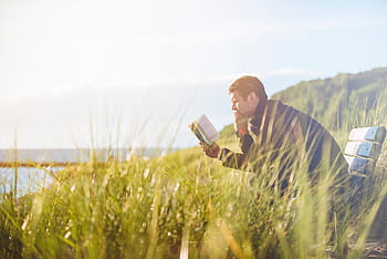 man, sitting, bench, holding, book, reading, outdoor, middle, grassfield, blue, white