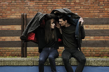 man, woman, sits, beige, concrete, bench, front, brick wall, brown, concrete road, daytime