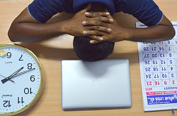 man, aan het liegen, beige, tafel, zilveren macbook, koperkleurige analoge klok, maandelijks, kalender, werk management, tijdsbeheer, kantoor