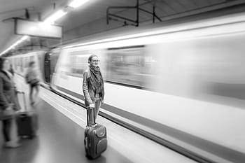 grayscale photo, woman, holding, trolley bag, gray, scale, portrait, standing, behind, train, station