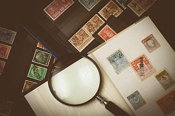 kolekce různých barevných poštovních známek, zvětšování, sklenka, stůl, filatelista, sbírka známek, razítko, sběr, sbírka, smyčka, zoom