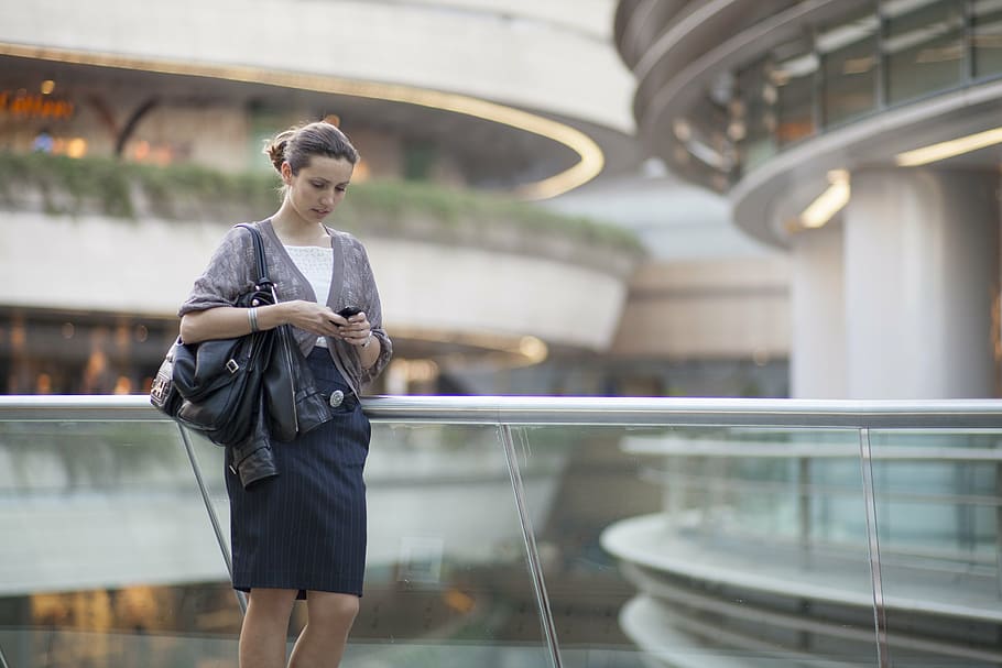 woman, grey, 3/4 sleeved blazer, black, skirt, holding, smartphone, leather, tote, bag, standing